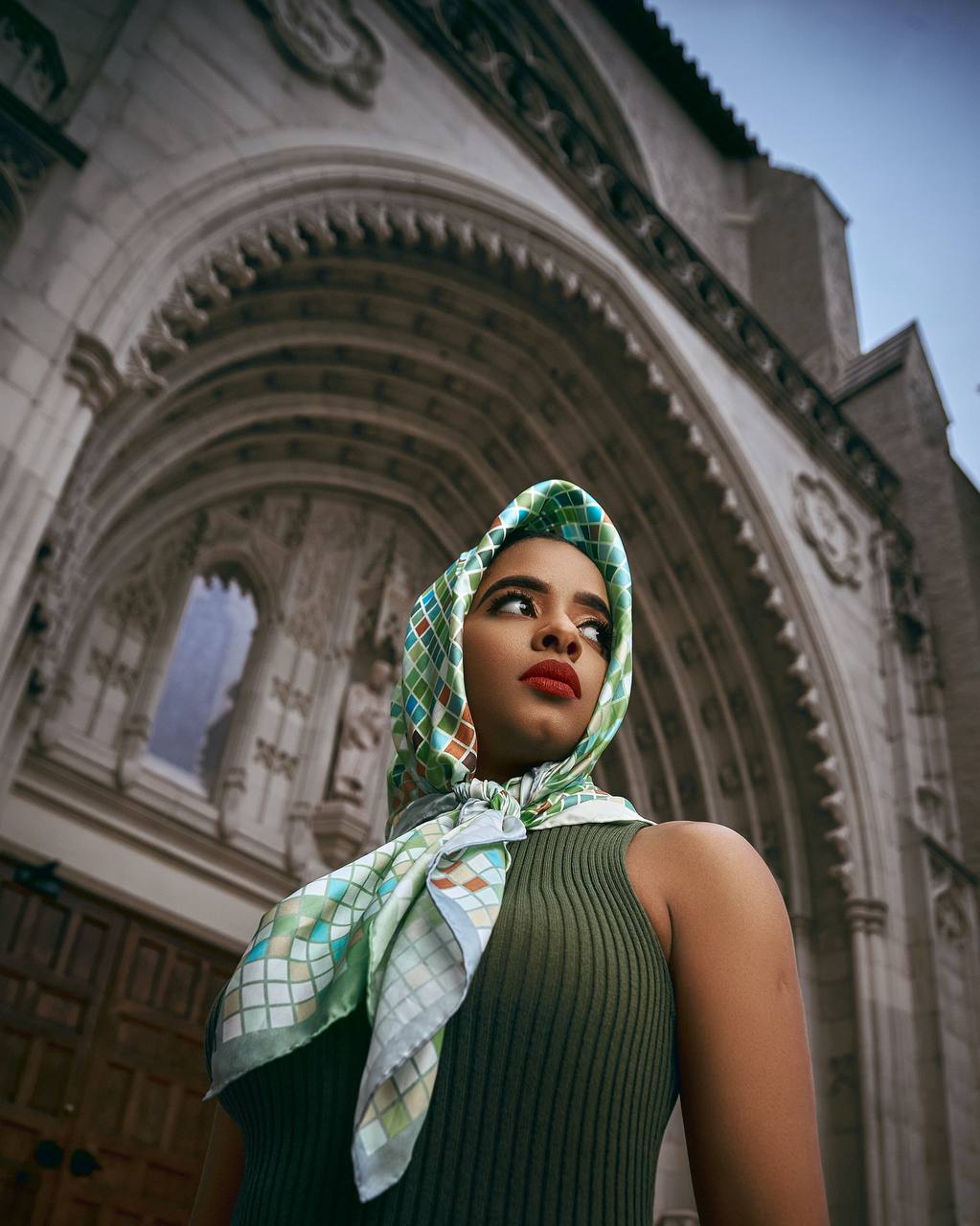 Editorial portrait of a woman in a patterned headscarf standing before ornate architecture