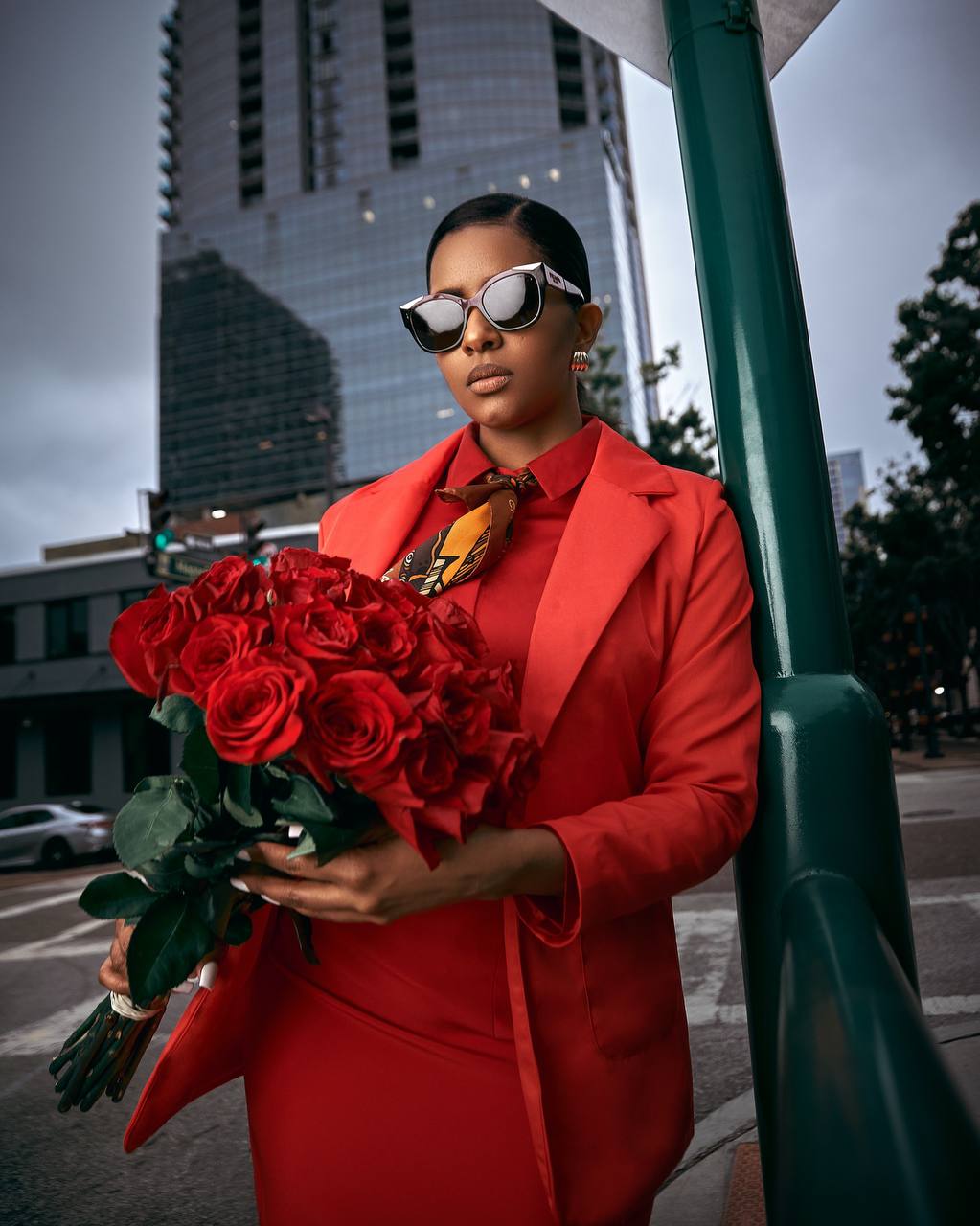 Street-style portrait of a woman in red holding a bouquet of roses in the city
