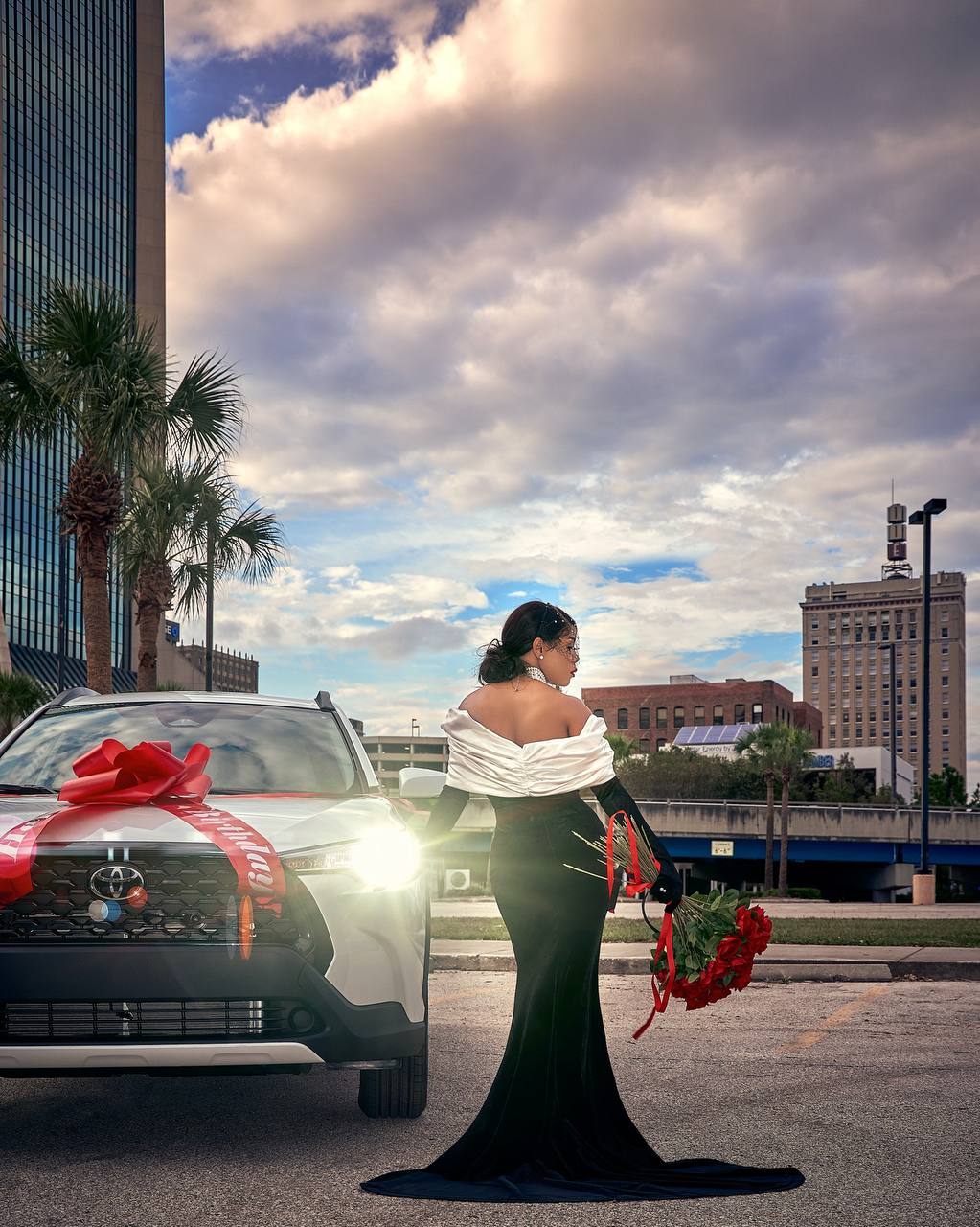 Wedding portrait of a woman in a black and white gown beside a decorated car at sunset